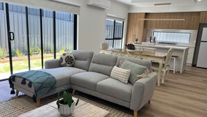 A modern living room with a sectional sofa, a dining area, and a kitchen. - The Cosy Cottage  (Ararat)