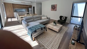 A modern living room with a grey sofa, wooden coffee table, and a dining area with a white table and chairs. - The Cosy Cottage  (Ararat)