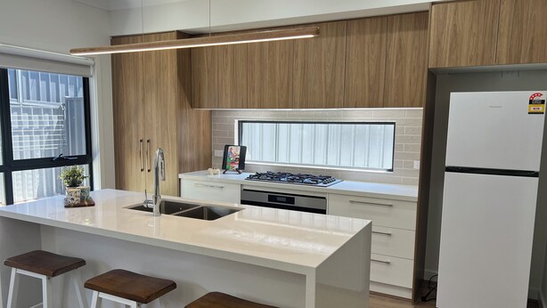 A modern kitchen with a central island, bar stools, a built-in stove, and a refrigerator. - The Cosy Cottage  (Ararat)