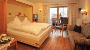 A bedroom with a bed, a chair, a sofa, a television, and a window with curtains.