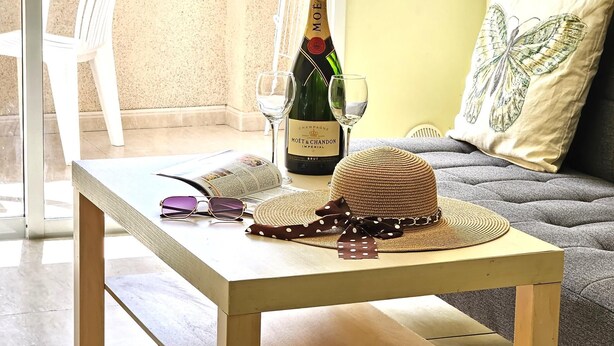 Une table avec une bouteille de champagne, un verre, un magazine et un chapeau de paille.
