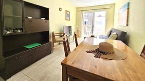 Un coin repas avec une table en bois, des chaises, un meuble avec des tiroirs, un téléviseur et une vue sur l’extérieur grâce à une porte vitrée.