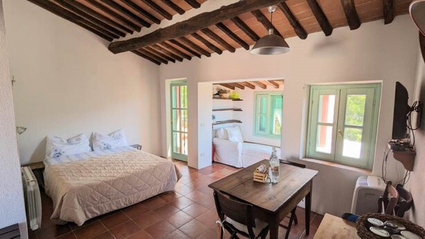 Ein Schlafzimmer mit einem Bett, einem Tisch und einem Stuhl. Es gibt ein Fenster mit grünen Rollläden und eine Heizung.