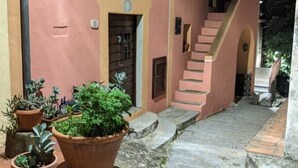 Eine schmale, gepflasterte Gasse, gesäumt von Gebäuden mit Terrakotta-Dächern, und eine Treppe, die zu einer höheren Ebene führt.