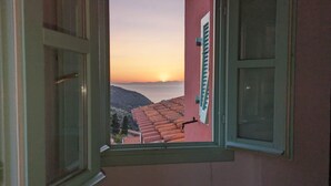 Blick aus dem Fenster auf Terrakotta-Dächer und einen Sonnenuntergang über einer Berglandschaft.