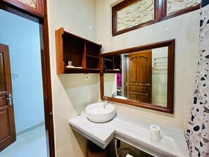 A bathroom with a white sink, a mirror, and a wooden cabinet above it. - Puri Karang Residence (Tembuku)