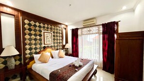 A hotel room with a large bed, wooden headboard, patterned wall, and a window with curtains. - Puri Karang Residence (Tembuku)