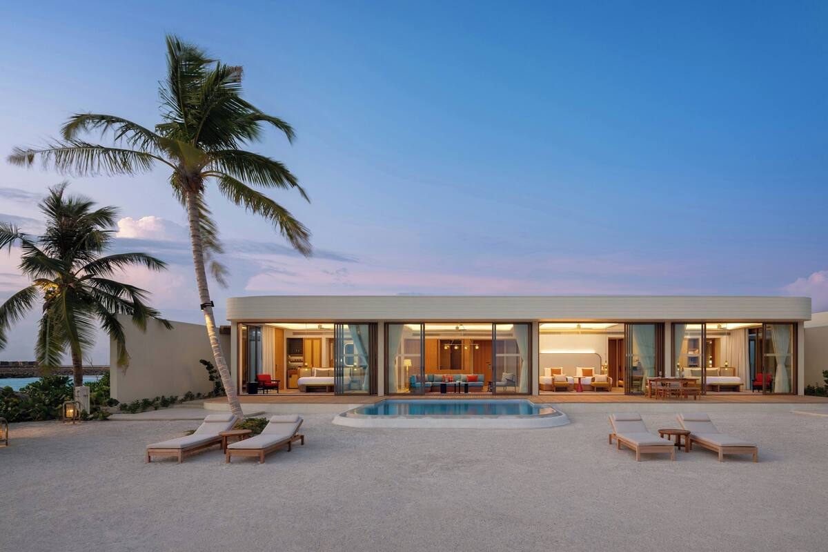 Un complexe hôtelier moderne doté d’une piscine, de chaises longues et d’une grande façade en verre.