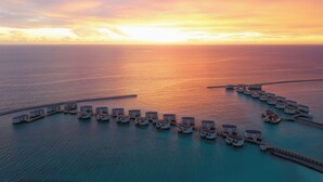 An aerial view of overwater bungalows connected by walkways, set against a sunset over the ocean. - Centara Grand Lagoon Maldives (Kodhipparu Falhu)