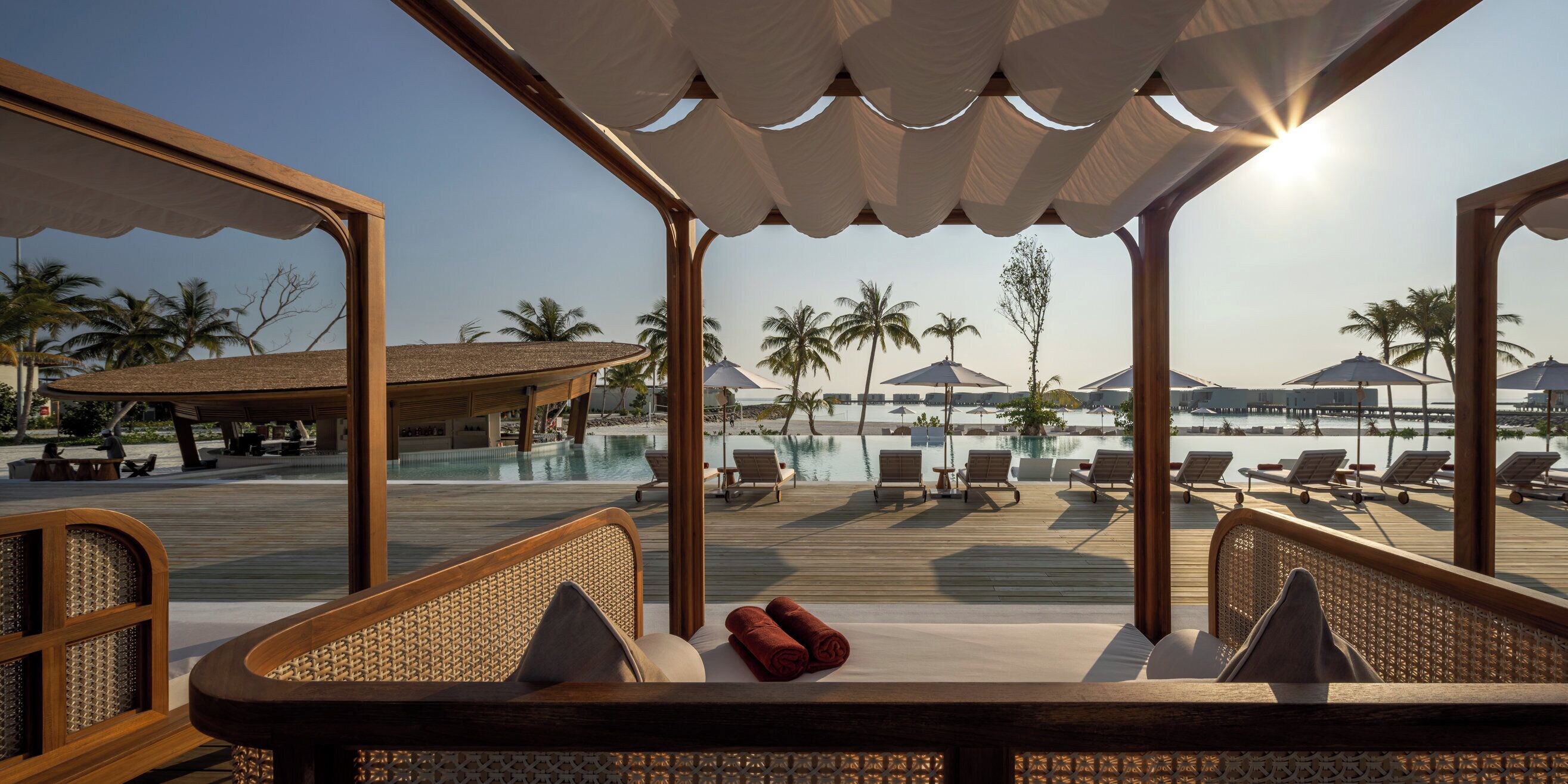 Ein Liegebereich am Pool mit Holzmöbeln und Blick auf Pool und Strand.