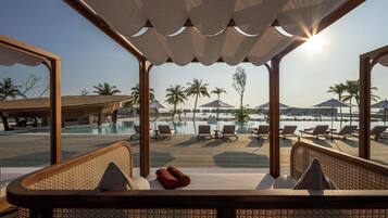Ein Liegebereich am Pool mit Holzmöbeln und Blick auf Pool und Strand.