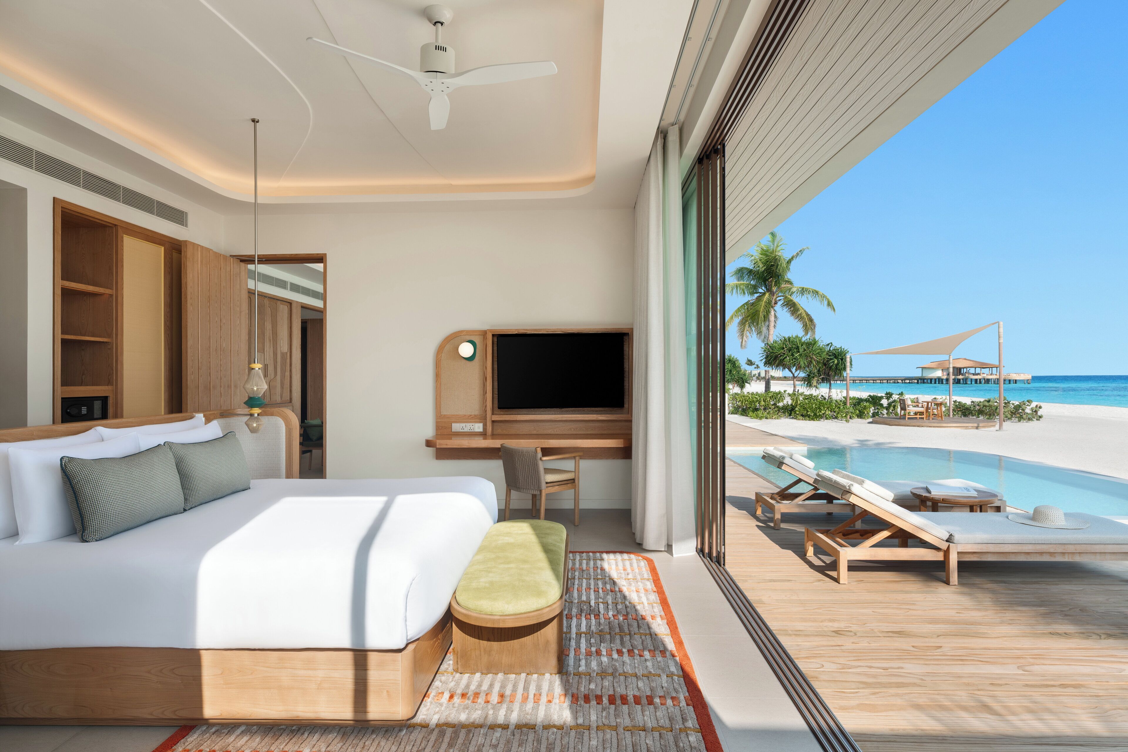 Habitación de hotel moderna con una cama grande, un escritorio, un televisor y vistas a la playa y la piscina.