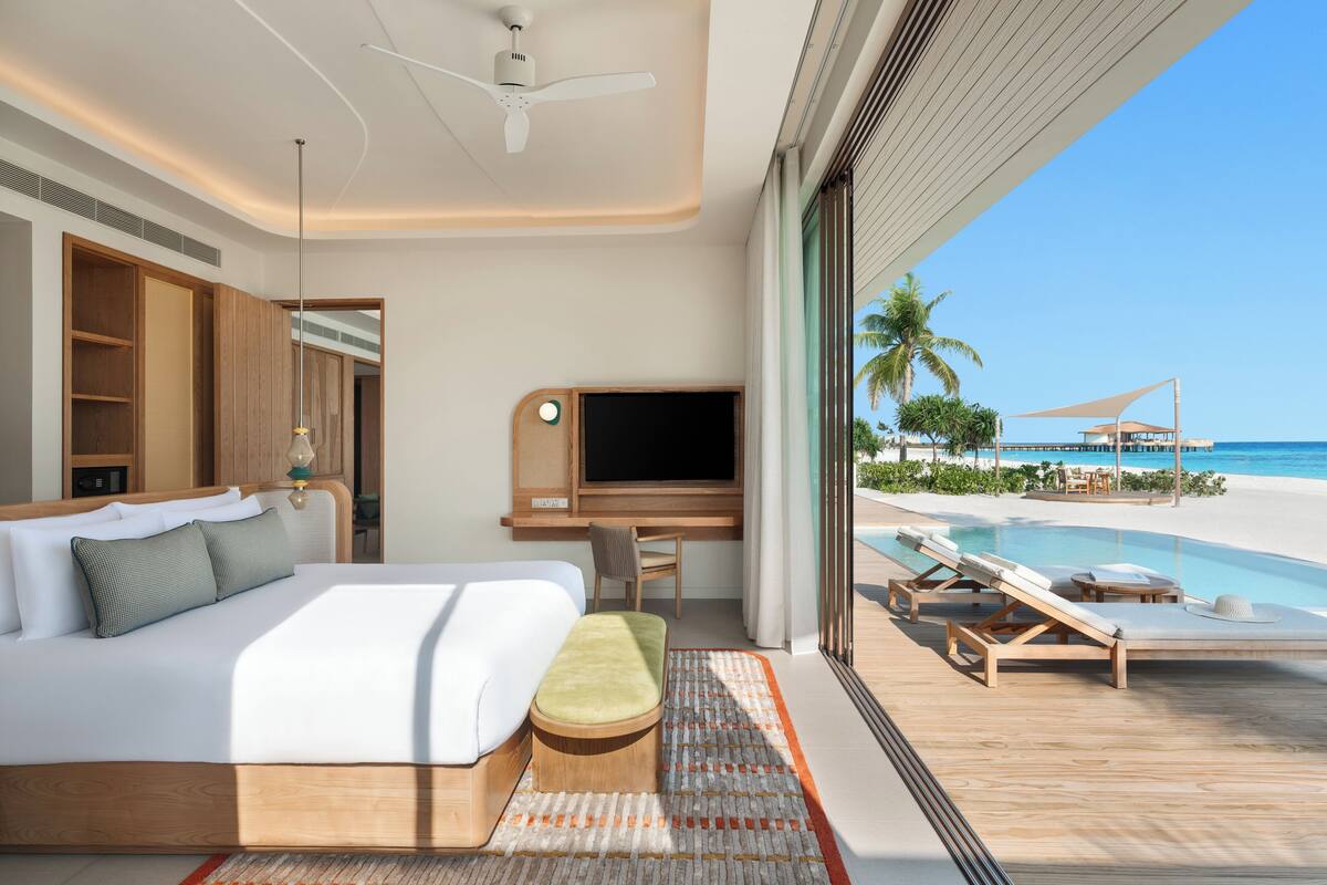 Une chambre d’hôtel moderne dotée d’un grand lit, d’un bureau, d’une télévision et offrant une vue sur la plage et la piscine.