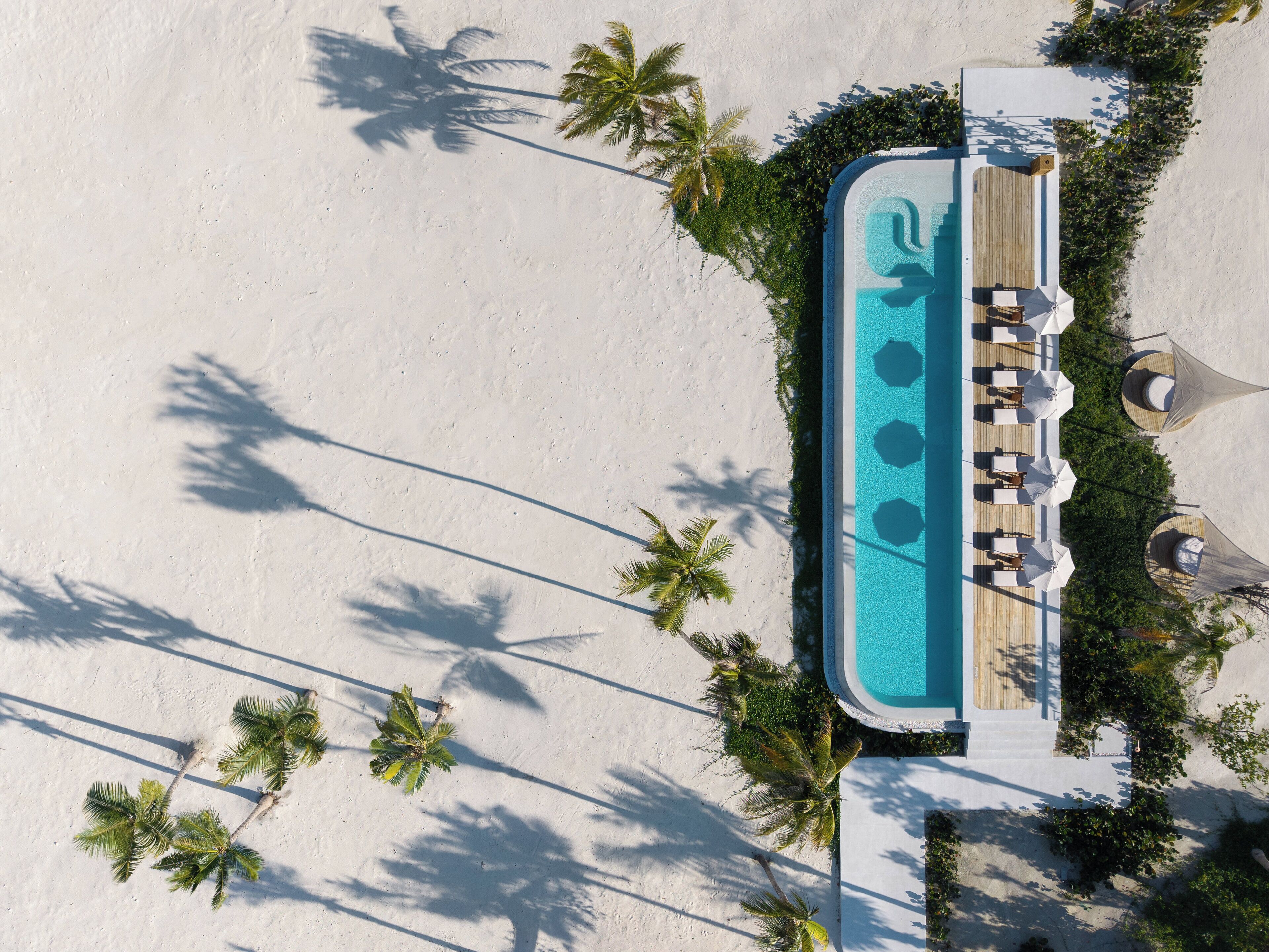 An aerial view of a resort with a swimming pool, lounge area, and palm trees.