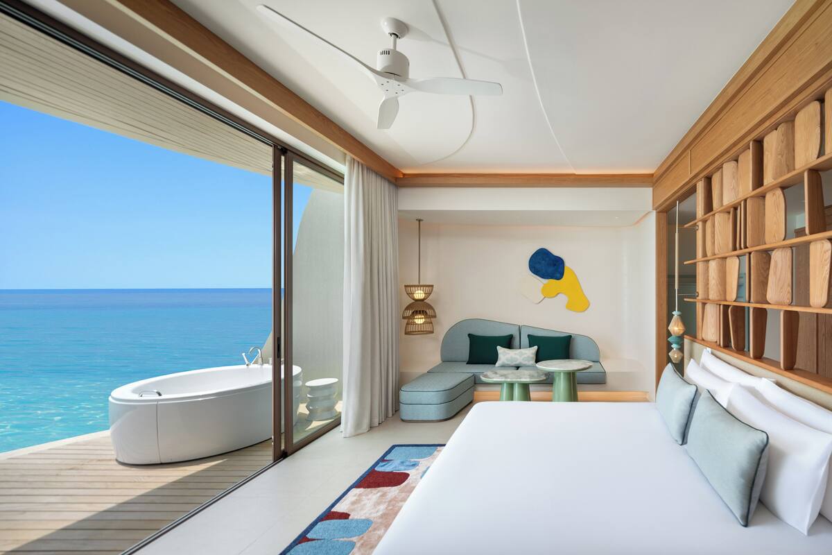 Ein modernes Zimmer mit einem großen Bett, einer Sitzecke, einer Badewanne und Meerblick.