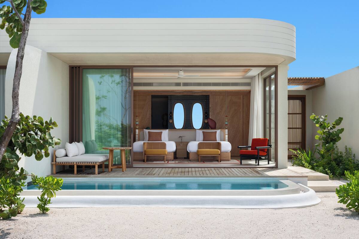 Un complexe hôtelier moderne doté d’une piscine, d’un coin salon avec deux canapés et une table, ainsi que d’une chambre séparée avec un lit et un fauteuil rouge.