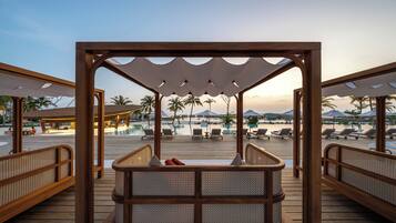 A wooden deck with a seating area overlooking a pool and beach.
