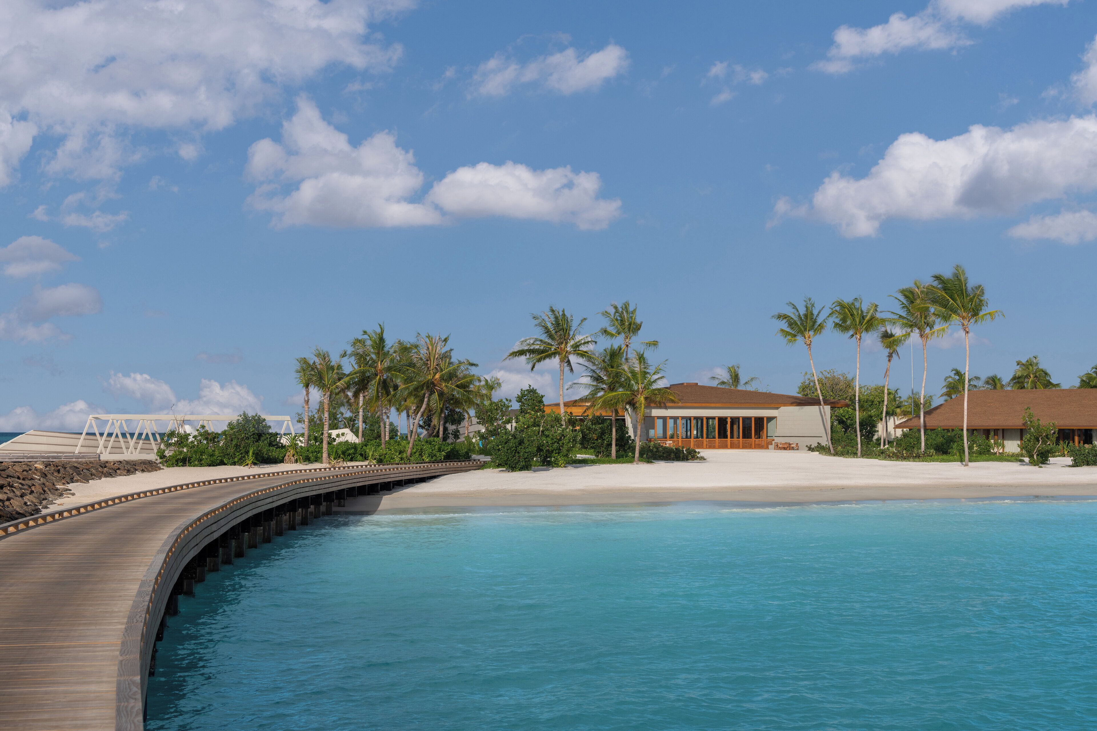 Un complejo turístico costero con un puente de madera, palmeras y villas frente a la playa.