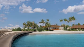 Un complejo turístico costero con un puente de madera, palmeras y villas frente a la playa.