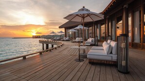 A wooden deck with outdoor seating and umbrellas overlooking a body of water at sunset. - Centara Grand Lagoon Maldives (Kodhipparu Falhu)