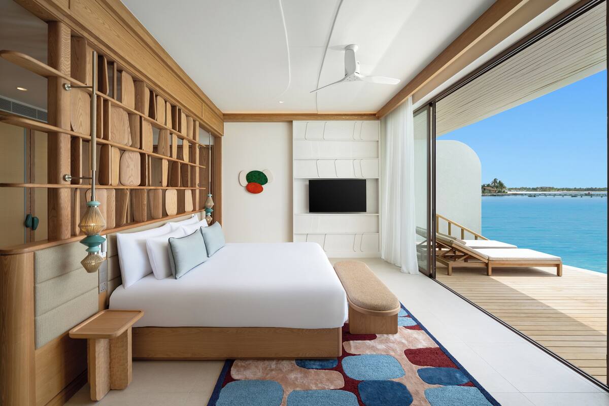 Ein modernes Schlafzimmer mit einem großen Bett, einem Holz-Kopfende, einem Flachbildfernseher und einem Balkon mit Meerblick.