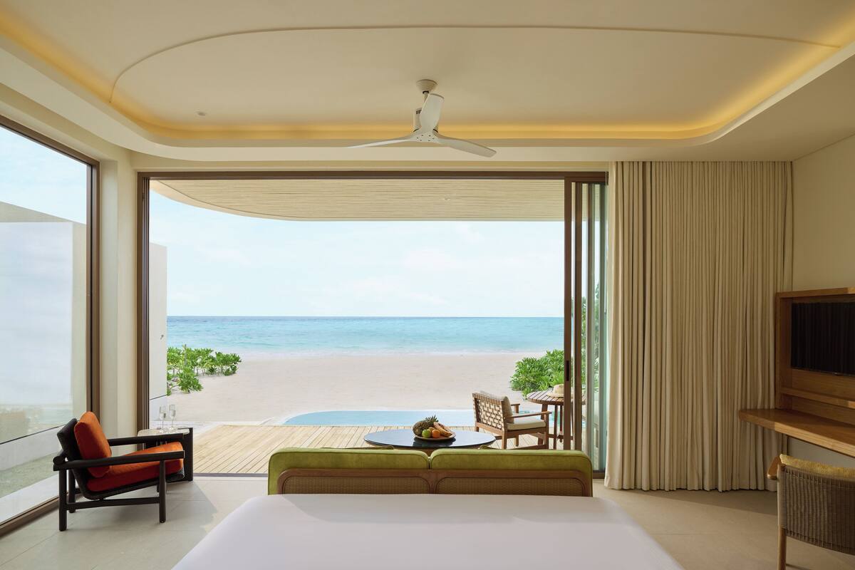 Ein Hotelzimmer mit einem großen Bett, einer Sitzecke mit Tisch, einem Fernseher und Blick auf den Strand.
