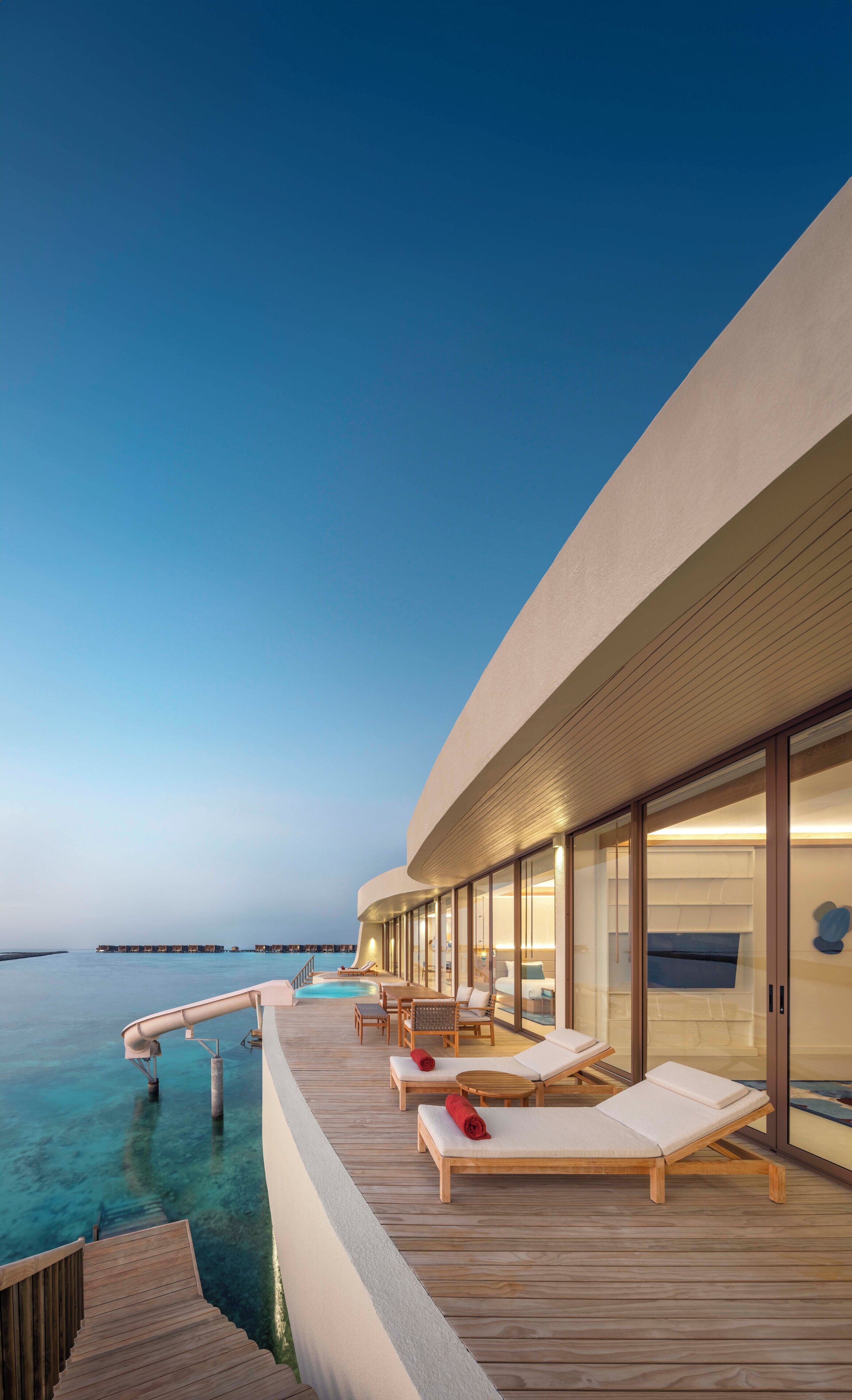 Un moderno resort con zona de piscina, sillones reclinables y vistas al océano.