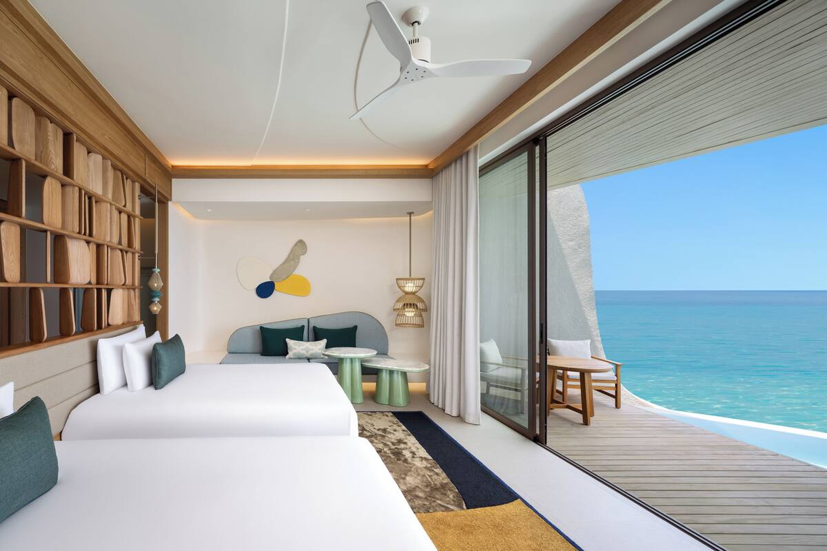 Ein modernes Hotelzimmer mit einem großen Bett, einer Sitzecke mit Tisch und Blick auf den Ozean.