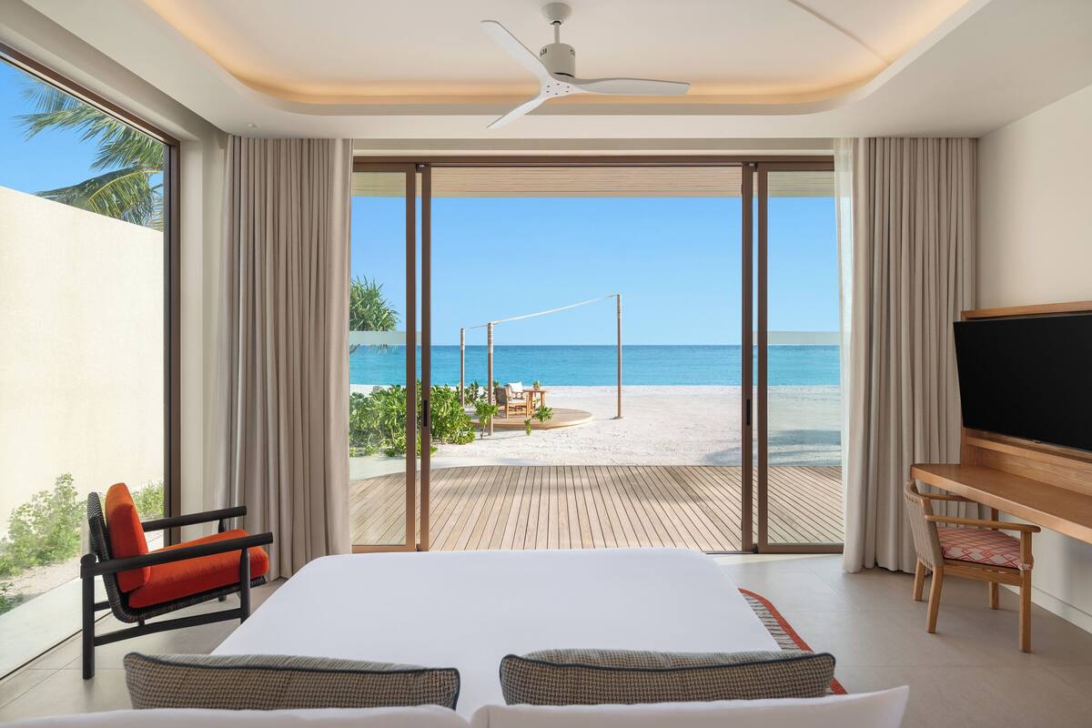 Ein Hotelzimmer mit einem großen Bett, einem Schreibtisch, einem Fernseher und Blick auf den Strand.