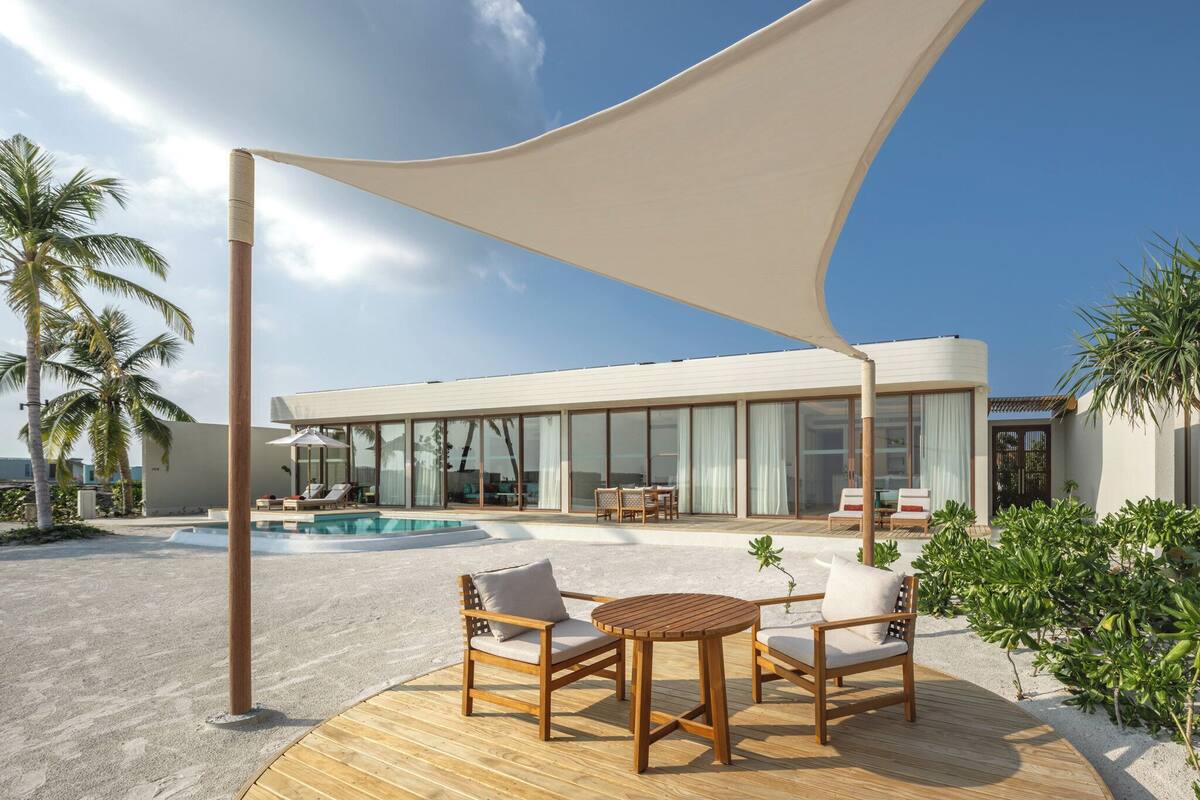 Ein moderner Außenbereich mit Pool, Palmen und einem zeitgemäßen Haus im Hintergrund.