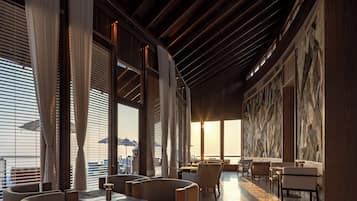 A modern interior with large windows, wooden ceiling beams, and a seating area with tables and chairs.