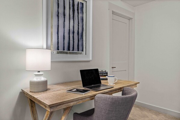 A small workspace with a wooden desk, a laptop, a lamp, a notebook, and a mug.