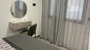 Une chambre à coucher avec un lit, une table de chevet, un miroir, une chaise et des rideaux légers.