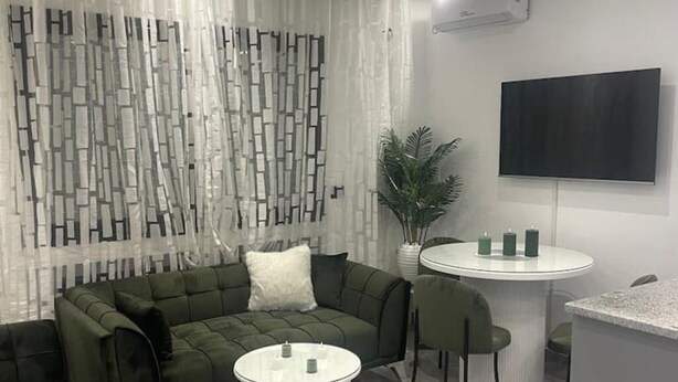 Un salon moderne avec un canapé d’angle, une table de salle à manger ronde et un téléviseur à écran plat fixé au mur.