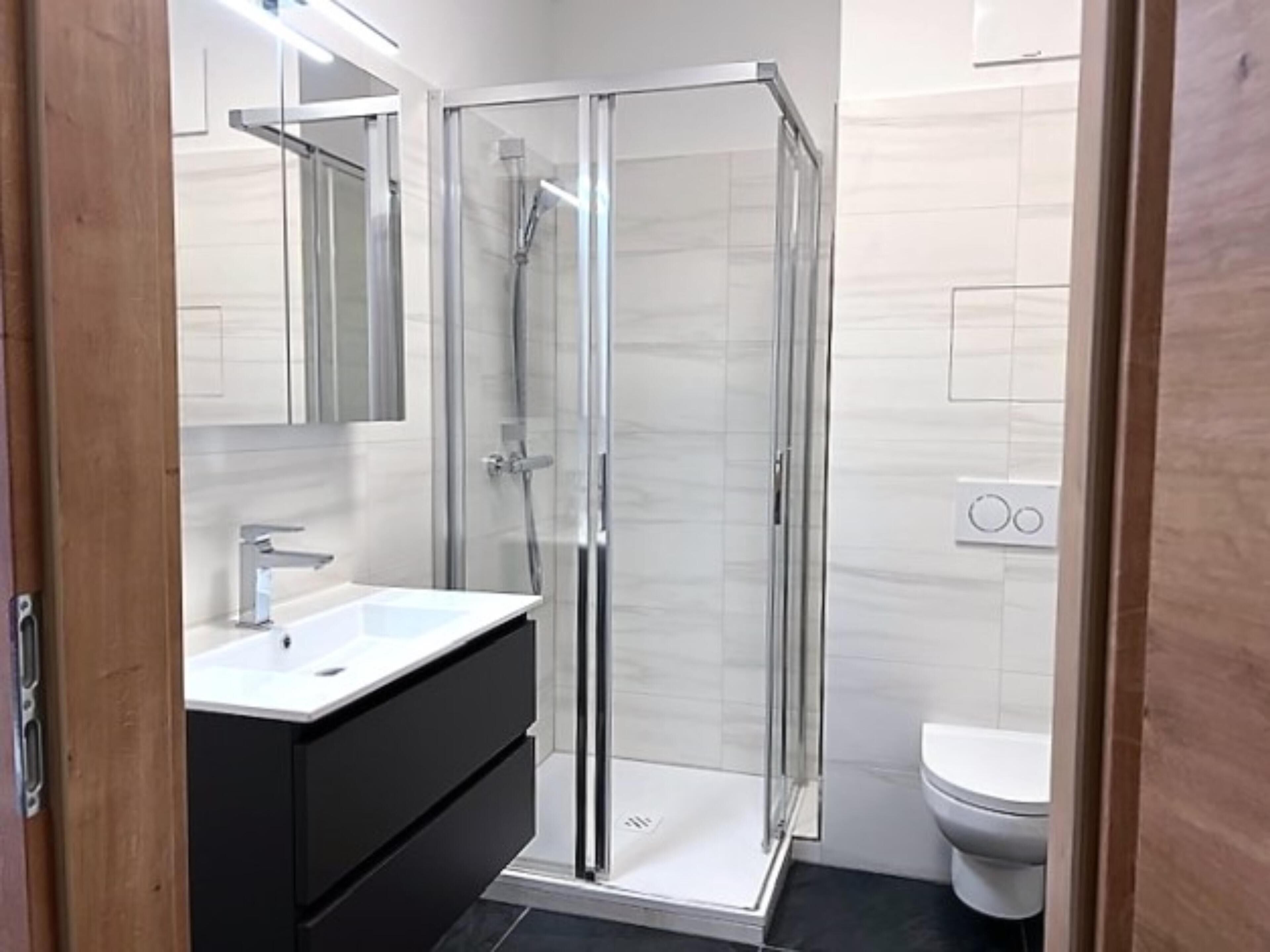 Ein modernes Badezimmer mit einer gläsernen Duschkabine, einem weißen Waschbecken und einer Toilette.