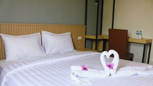 Habitación de hotel con cama, almohadas, cabecera de madera, escritorio con silla y una botella de agua en el escritorio.