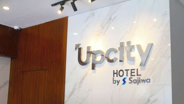 Señalización de 'Upcity Hotel by Sajiwa' con un fondo de pared de mármol y paneles de madera.