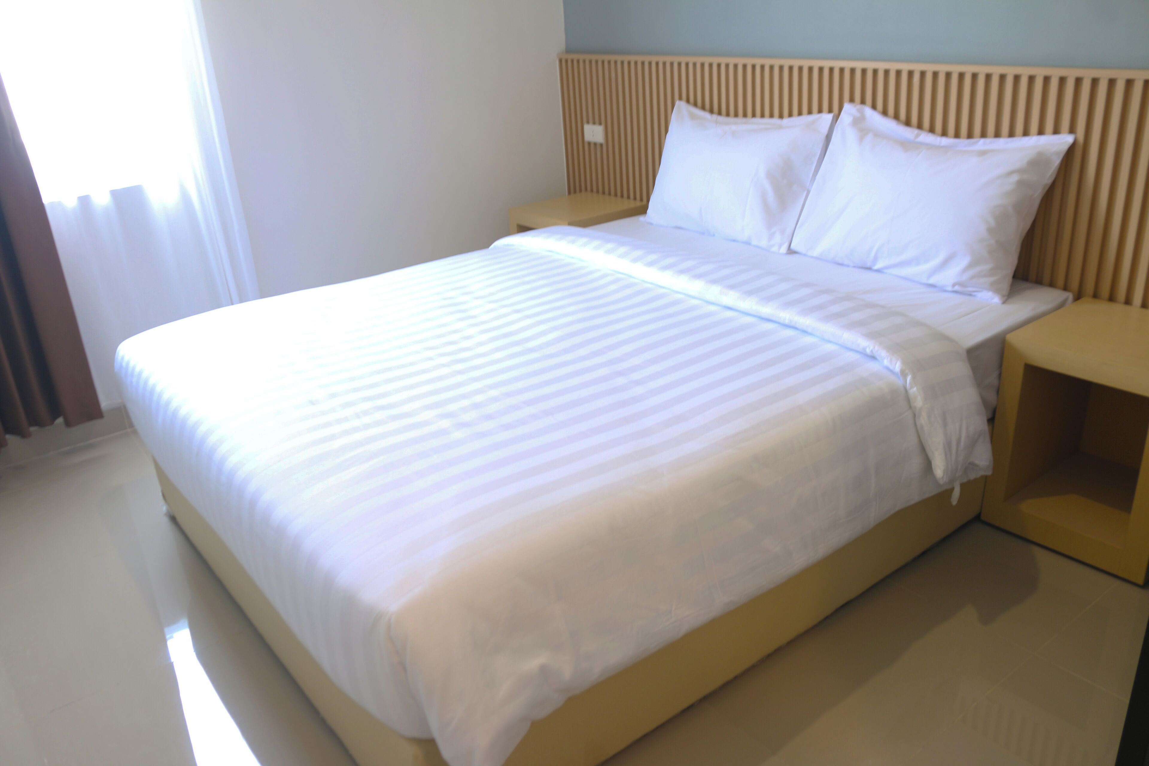 A neatly made bed with white linens, a wooden headboard, and a bedside table.