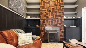 A modern living room with a brown leather sofa, a fireplace, and a wooden accent wall. - Barkly Terrace | Carlton's Charming Heritage (Carlton)