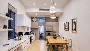 A modern kitchen with a wooden dining table, white cabinetry, and a clock on the wall. - Barkly Terrace | Carlton's Charming Heritage (Carlton)