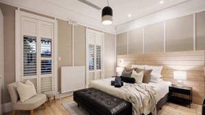 A bedroom with a bed, a chair, a bench, a nightstand, and a radiator. - Barkly Terrace | Carlton's Charming Heritage (Carlton)