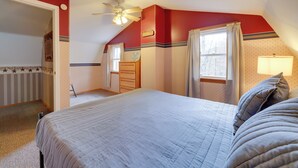 A bedroom with a large bed, a ceiling fan, a dresser, and a window with curtains.