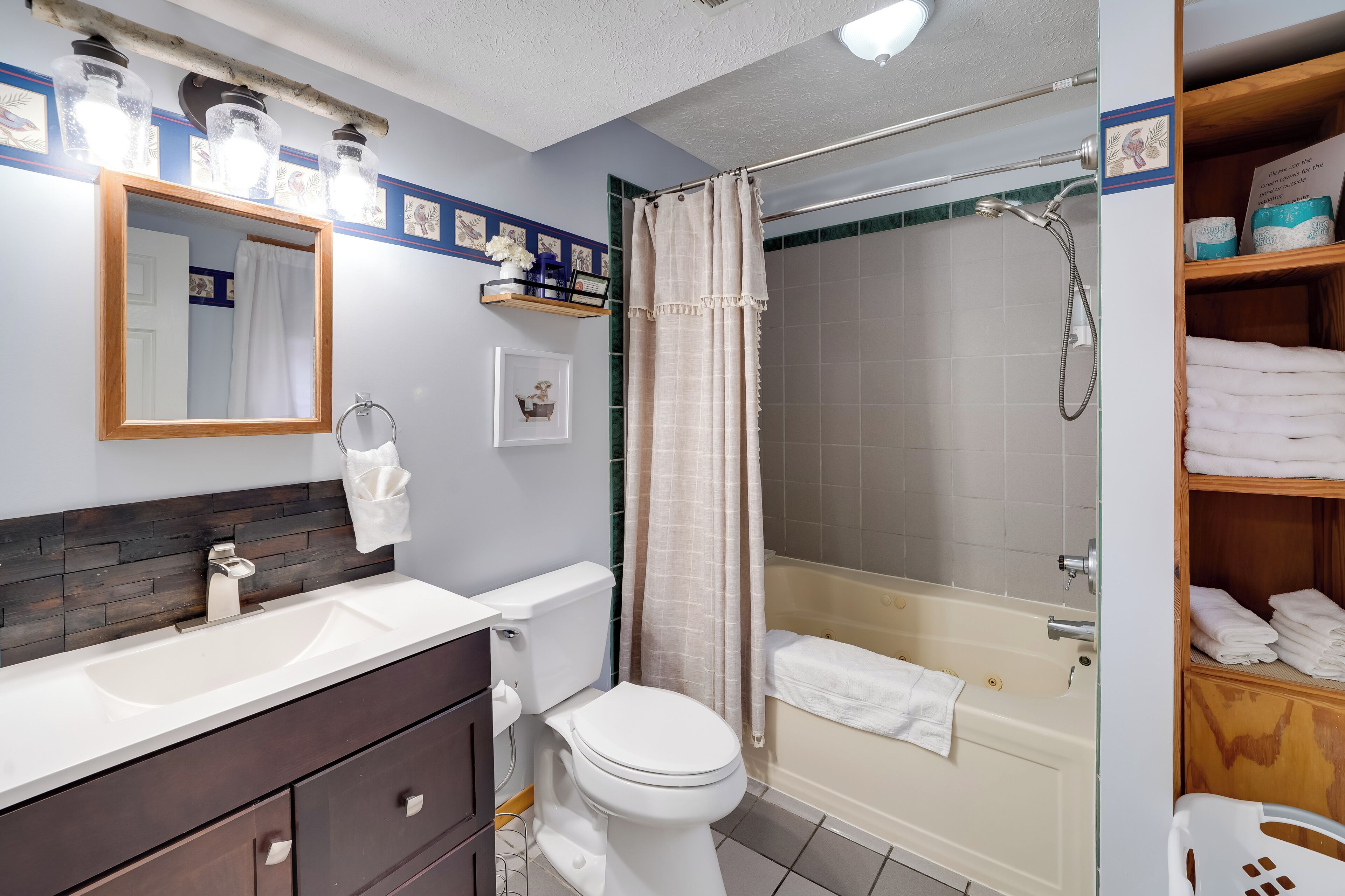 A bathroom with a white sink, dark wooden vanity, a white toilet, a shower with a beige curtain, and a bathtub with a white towel.