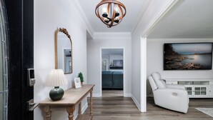 Ein modernes Wohnzimmer mit Holzboden, einem weißen Sofa, einem großen Gemälde und einer Deckenleuchte.