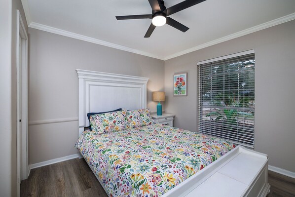 A bedroom with a bed, a ceiling fan, a window with blinds, a nightstand, and a lamp.