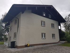 Ein zweistöckiges Gebäude mit geneigtem Dach, mehreren Fenstern und einer gepflasterten Auffahrt.