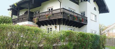 A two-story house with a balcony, surrounded by greenery.