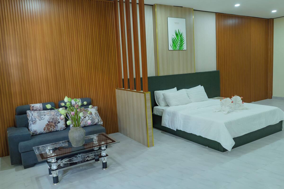 A modern hotel room with a sofa, a bed, a coffee table, and a decorative vase.