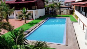 A rectangular swimming pool with a wooden deck surrounding it, set in a landscaped area with palm trees and a red-tiled patio. - Peaceful Hotel (Vientiane)
