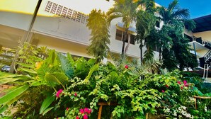A building with a white facade, surrounded by lush greenery and palm trees. - Peaceful Hotel (Vientiane)